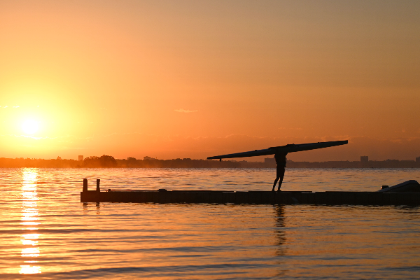 Athlete carying sprint boat off dock after sunrise practice 