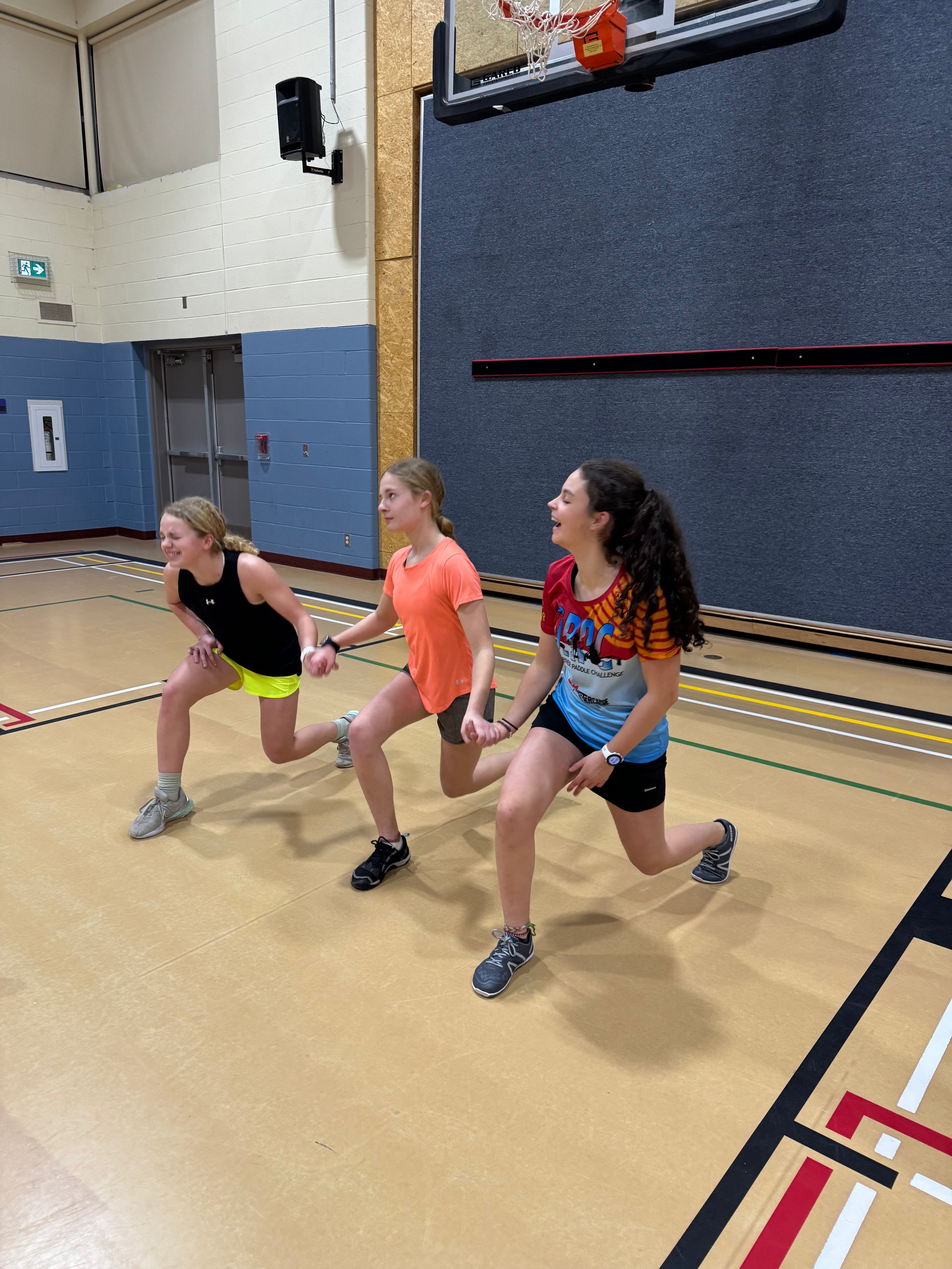 U16 female athletes do lunges together in a school gym as part of winter training.