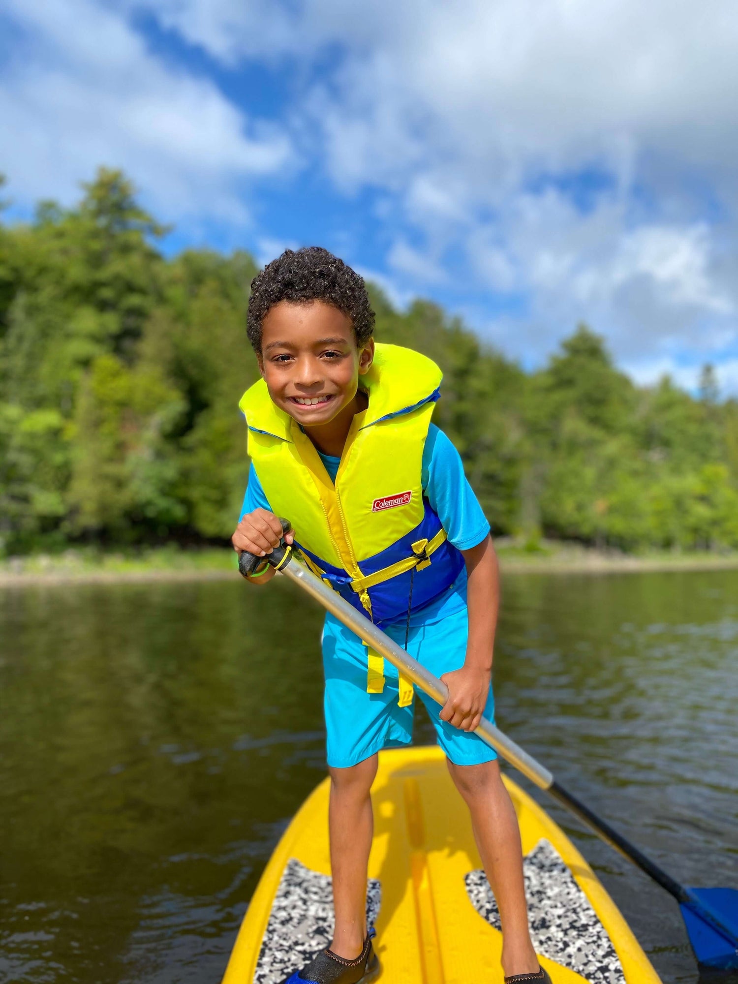 Young camper smiling while having fun on his own SUP while floating on the river.